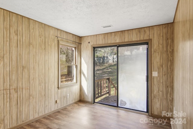 unfurnished room with light hardwood / wood-style floors, a textured ceiling, and wooden walls