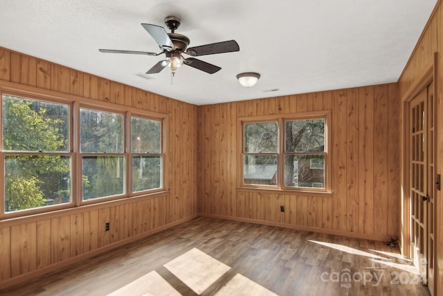 empty room featuring ceiling fan, light hardwood / wood-style flooring, a wealth of natural light, and wood walls