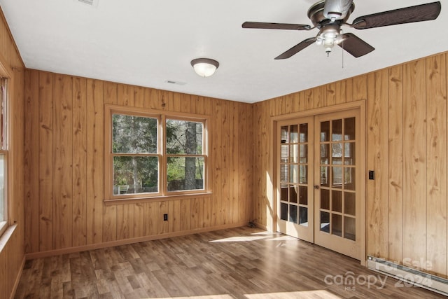 unfurnished room with ceiling fan, french doors, a baseboard heating unit, wood walls, and hardwood / wood-style floors