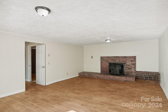 unfurnished living room with light wood-type flooring, a textured ceiling, and a wood stove