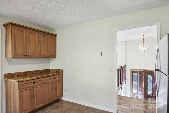 821 Anne Ave W, Hendersonville, NC 28739 - kitchen featuring freestanding refrigerator, a chandelier, brown cabinetry, tile patterned flooring, and a textured ceiling