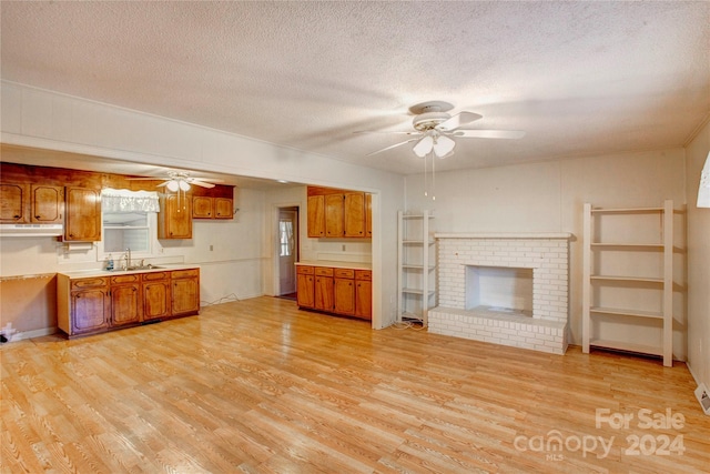 kitchen with a fireplace, a textured ceiling, sink, ceiling fan, and light hardwood / wood-style flooring