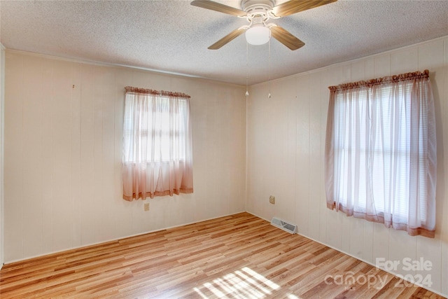 empty room with light wood-type flooring, wood walls, and ceiling fan