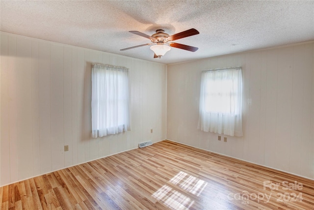 empty room with a textured ceiling, light wood-type flooring, wooden walls, and ceiling fan