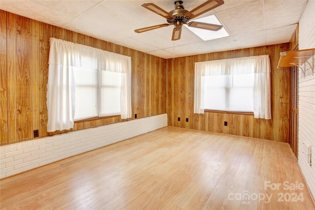 empty room featuring wood walls, wood-type flooring, ceiling fan, and plenty of natural light