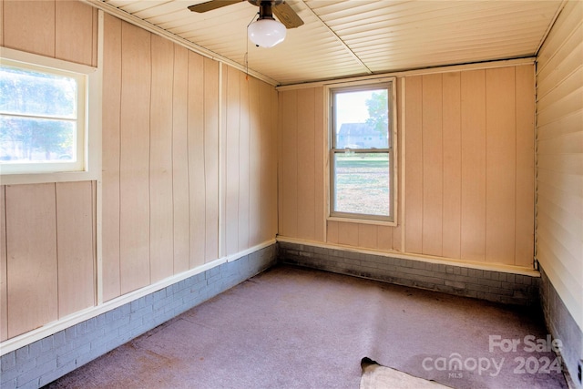 carpeted empty room with ceiling fan, wooden walls, brick wall, and wood ceiling