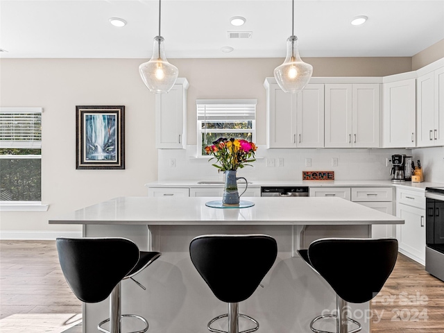 kitchen featuring white cabinets, a breakfast bar area, a kitchen island, pendant lighting, and light hardwood / wood-style flooring