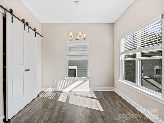 unfurnished dining area featuring dark hardwood / wood-style flooring, a barn door, and a notable chandelier