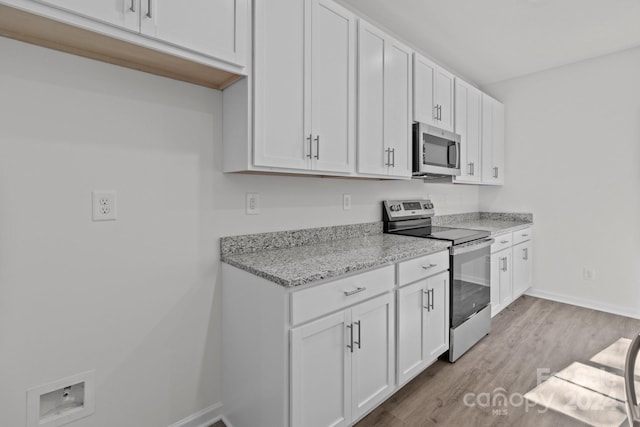 kitchen with appliances with stainless steel finishes, white cabinets, light stone counters, and light wood-type flooring