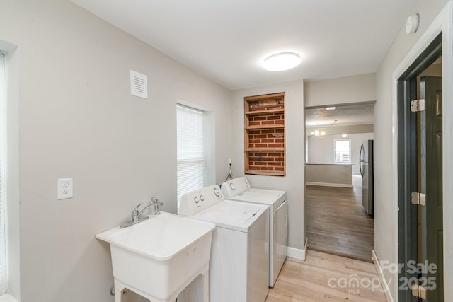 laundry room with visible vents, washing machine and clothes dryer, laundry area, a sink, and light wood-type flooring