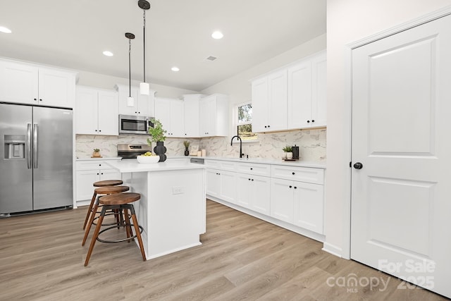 kitchen with stainless steel appliances, a kitchen island, hanging light fixtures, and white cabinetry