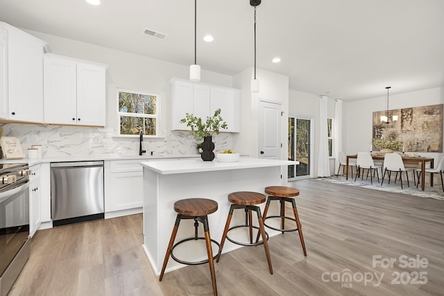 kitchen with white cabinetry, a center island, hanging light fixtures, stainless steel appliances, and backsplash