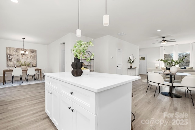 kitchen featuring white cabinets, decorative light fixtures, a kitchen island, and ceiling fan with notable chandelier