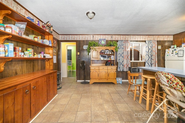 kitchen featuring a textured ceiling, white refrigerator, a kitchen breakfast bar, and light tile patterned flooring