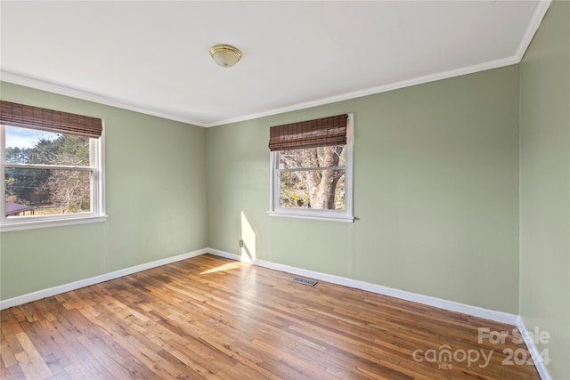 empty room featuring hardwood / wood-style flooring, a wealth of natural light, and ornamental molding