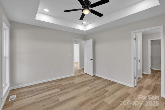 unfurnished bedroom featuring a raised ceiling, ceiling fan, and light wood-type flooring