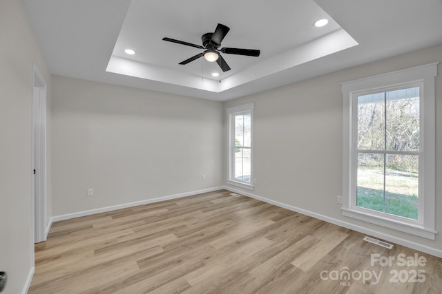 unfurnished room featuring ceiling fan, a tray ceiling, a wealth of natural light, and light wood-type flooring