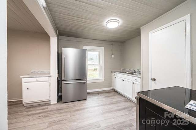 kitchen with stainless steel refrigerator, white cabinetry, sink, and light hardwood / wood-style floors