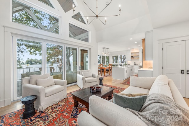 living room featuring plenty of natural light, light wood-type flooring, high vaulted ceiling, and a chandelier