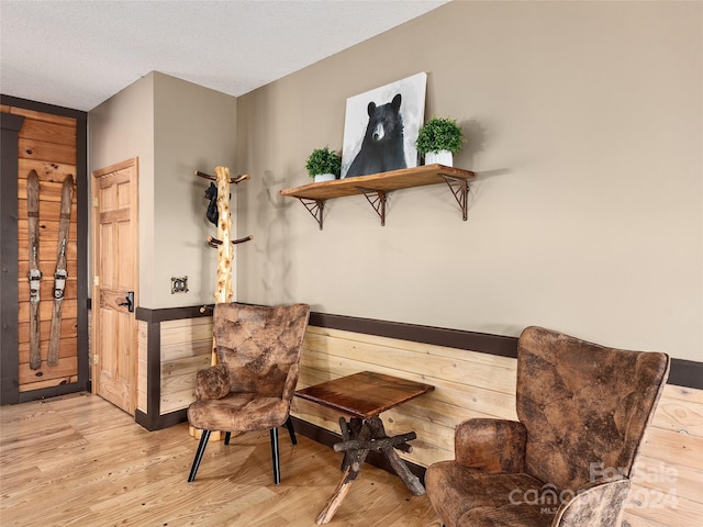 living area with light hardwood / wood-style floors, wooden walls, and a textured ceiling