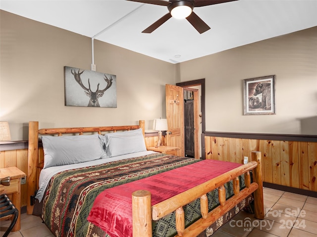 bedroom featuring wooden walls, ceiling fan, and light tile patterned floors