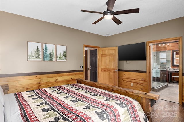 bedroom featuring ceiling fan, ensuite bath, hardwood / wood-style floors, and wood walls