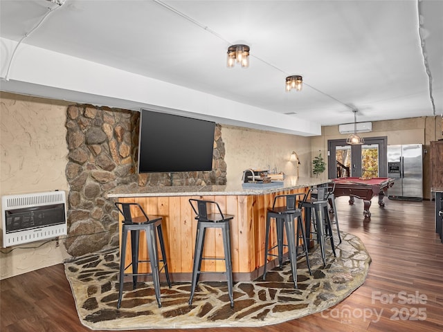 bar with dark wood-type flooring, stainless steel refrigerator with ice dispenser, heating unit, a fireplace, and an AC wall unit