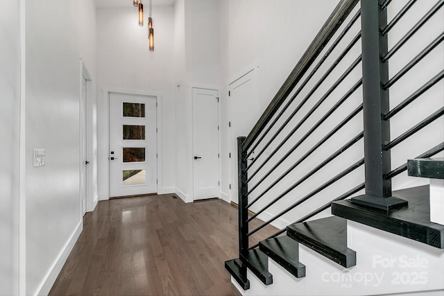 entrance foyer with dark wood-type flooring, baseboards, stairway, and a towering ceiling