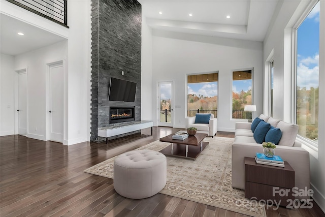 living area featuring baseboards, wood finished floors, a high ceiling, a fireplace, and recessed lighting