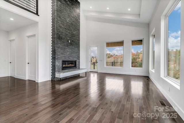 unfurnished living room with dark wood-style flooring, visible vents, a stone fireplace, and baseboards