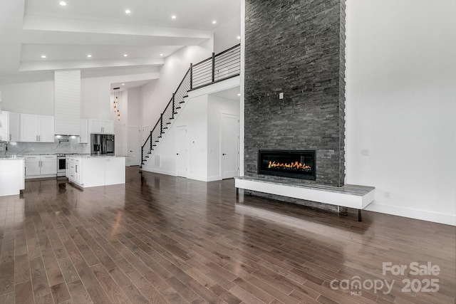 unfurnished living room with a fireplace, dark wood finished floors, a high ceiling, and stairs