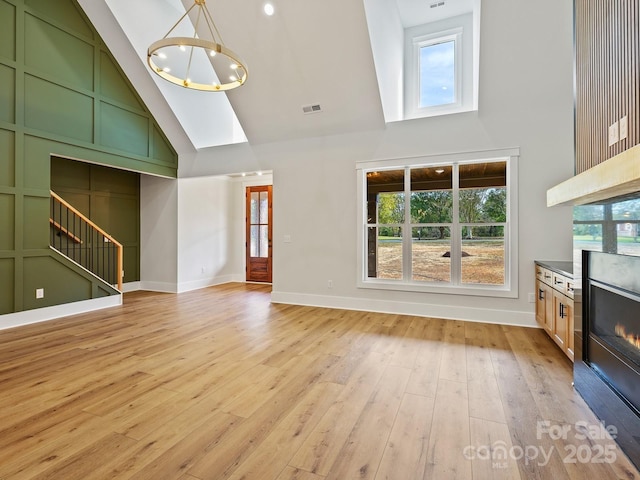 unfurnished living room with high vaulted ceiling, an inviting chandelier, and light hardwood / wood-style floors