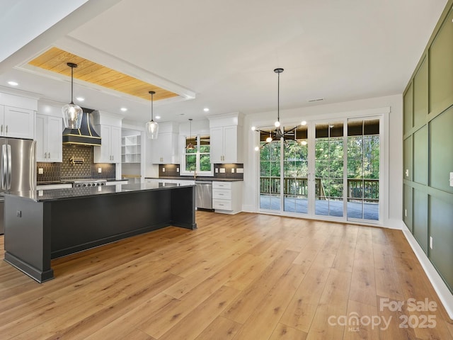 kitchen with appliances with stainless steel finishes, custom range hood, a kitchen island, decorative light fixtures, and white cabinets