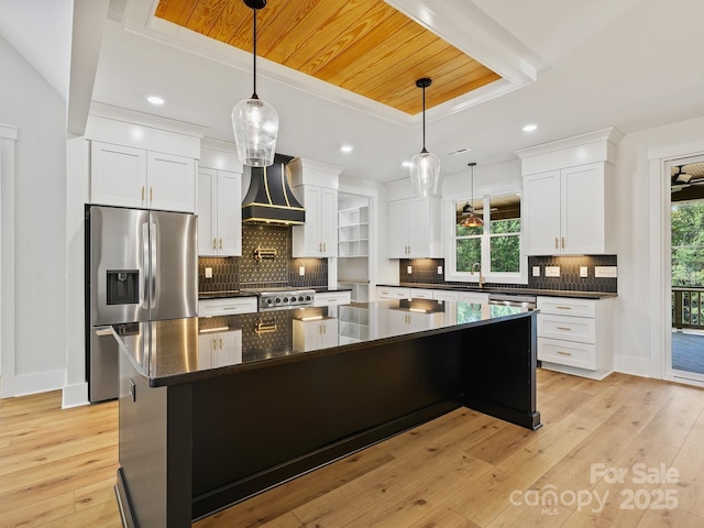 kitchen featuring premium range hood, a tray ceiling, a kitchen island, stainless steel fridge with ice dispenser, and white cabinets