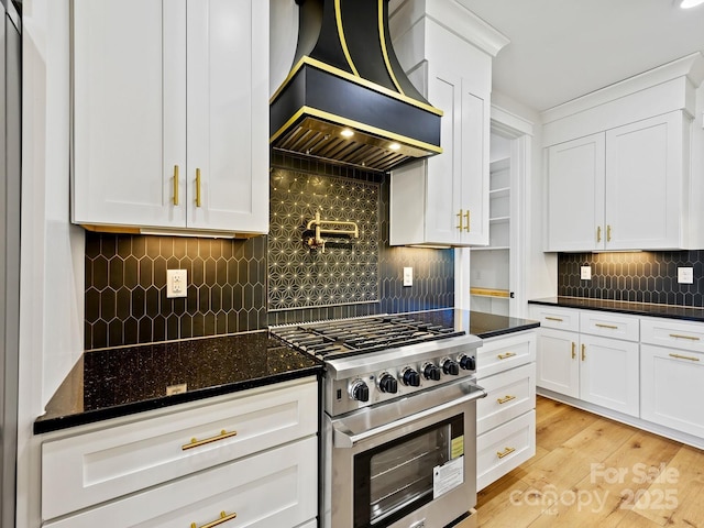 kitchen featuring custom range hood, white cabinets, light wood-type flooring, stainless steel range, and dark stone countertops