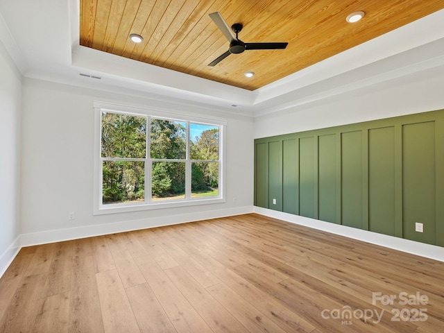 spare room with a tray ceiling, light hardwood / wood-style flooring, wood ceiling, and ceiling fan