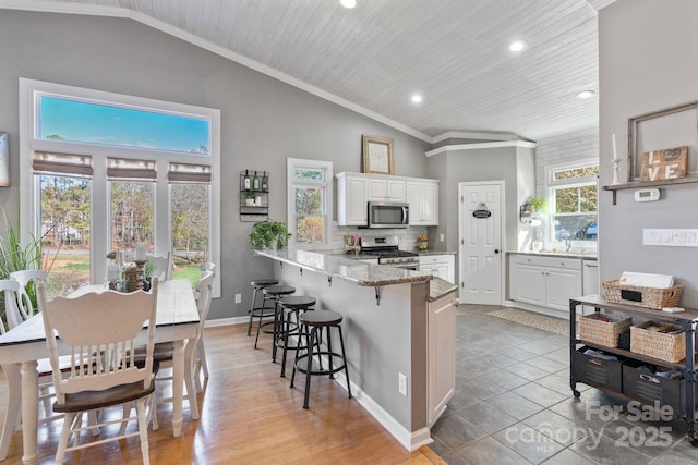 kitchen with light stone countertops, a kitchen breakfast bar, stainless steel appliances, white cabinets, and lofted ceiling