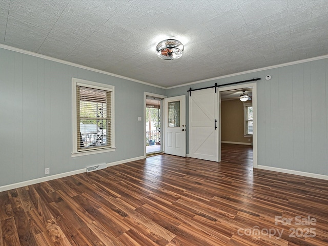 spare room featuring crown molding, dark wood-type flooring, and a barn door