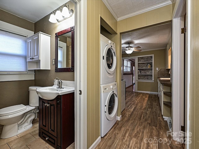 laundry area featuring hardwood / wood-style floors, stacked washer / drying machine, sink, ceiling fan, and crown molding