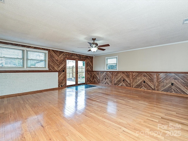 spare room featuring crown molding, wood walls, light wood-type flooring, and a textured ceiling