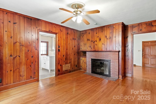 unfurnished living room with light wood-type flooring, a brick fireplace, ceiling fan, and wood walls