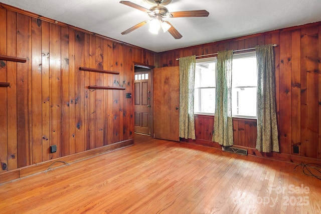 empty room with light wood-type flooring, ceiling fan, and wood walls