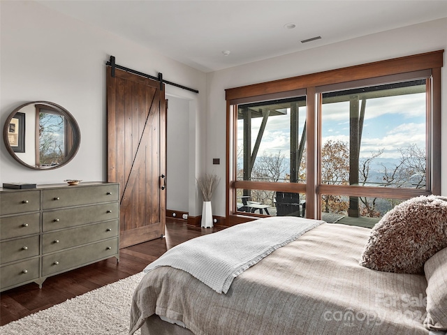 bedroom with a barn door and dark hardwood / wood-style flooring