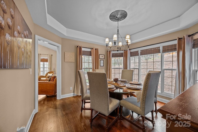 dining area featuring dark wood-type flooring, a notable chandelier, and a tray ceiling