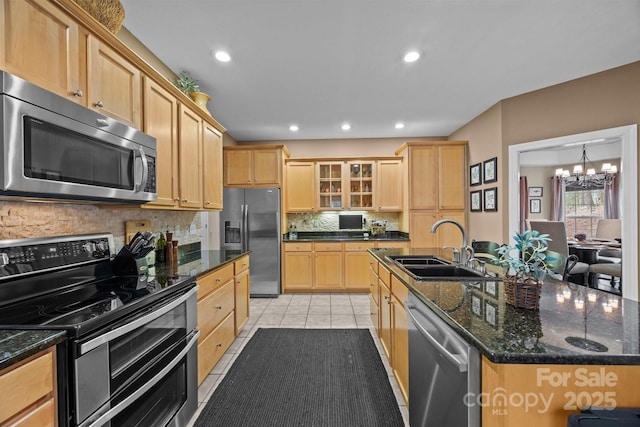 kitchen featuring appliances with stainless steel finishes, sink, backsplash, light tile patterned floors, and a center island with sink