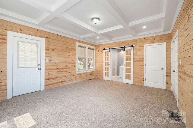 unfurnished bedroom with beamed ceiling, coffered ceiling, a barn door, and wood walls