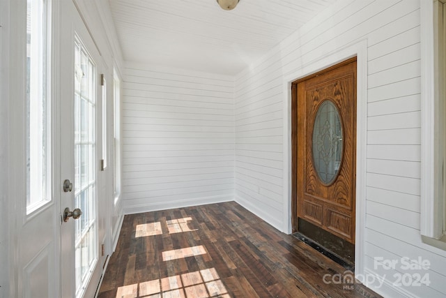 foyer entrance with dark wood-type flooring and wooden walls