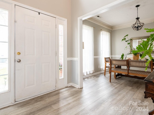 foyer with light hardwood / wood-style floors, a chandelier, a textured ceiling, and ornamental molding