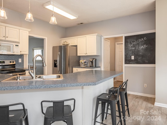 kitchen featuring stainless steel appliances, light hardwood / wood-style floors, sink, a breakfast bar area, and white cabinets