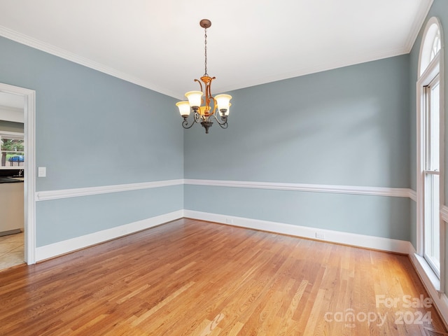 spare room with crown molding, an inviting chandelier, and light wood-type flooring